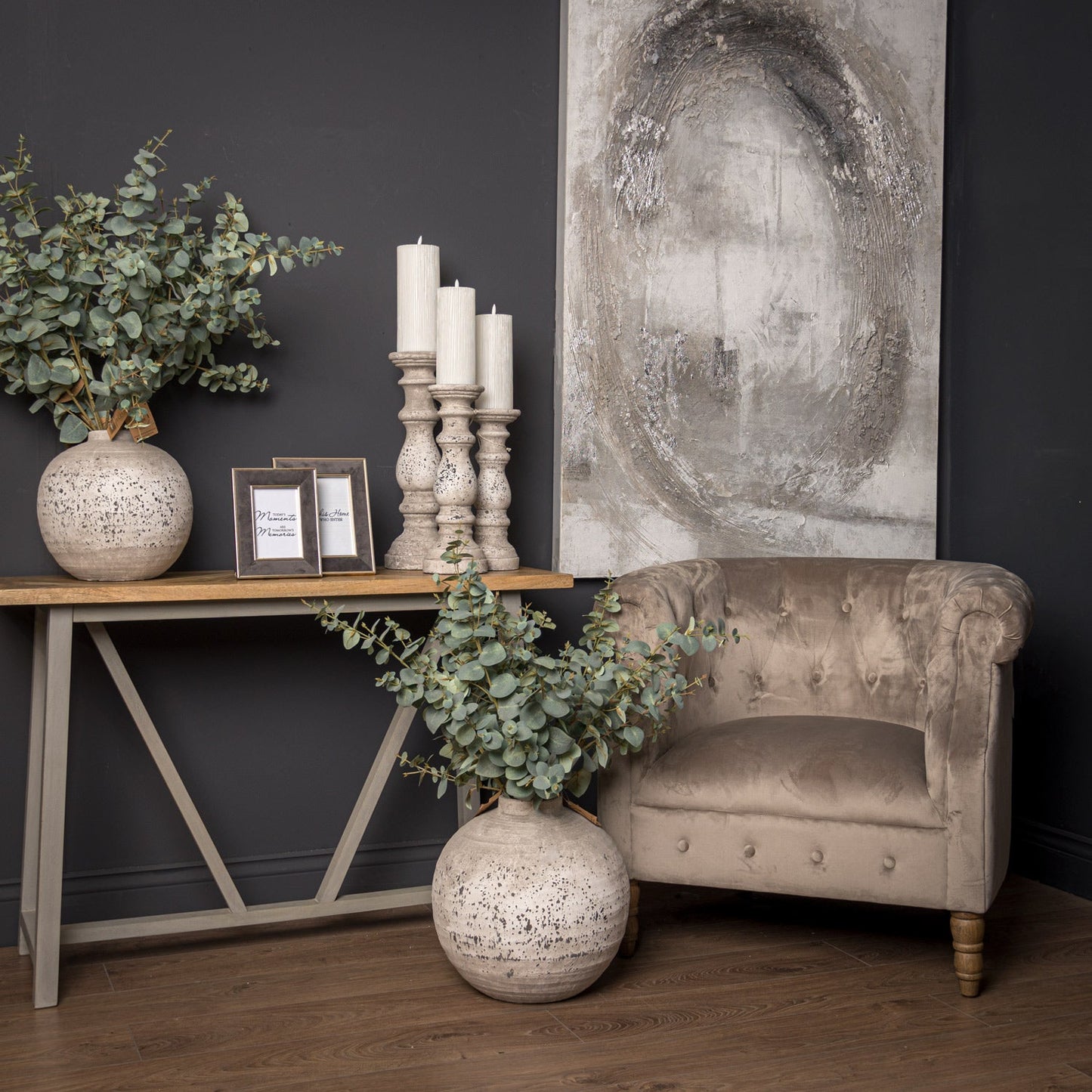 Aged stone vase and matching candlesticks on top of console table. Another vase on the floor next to velvet chair