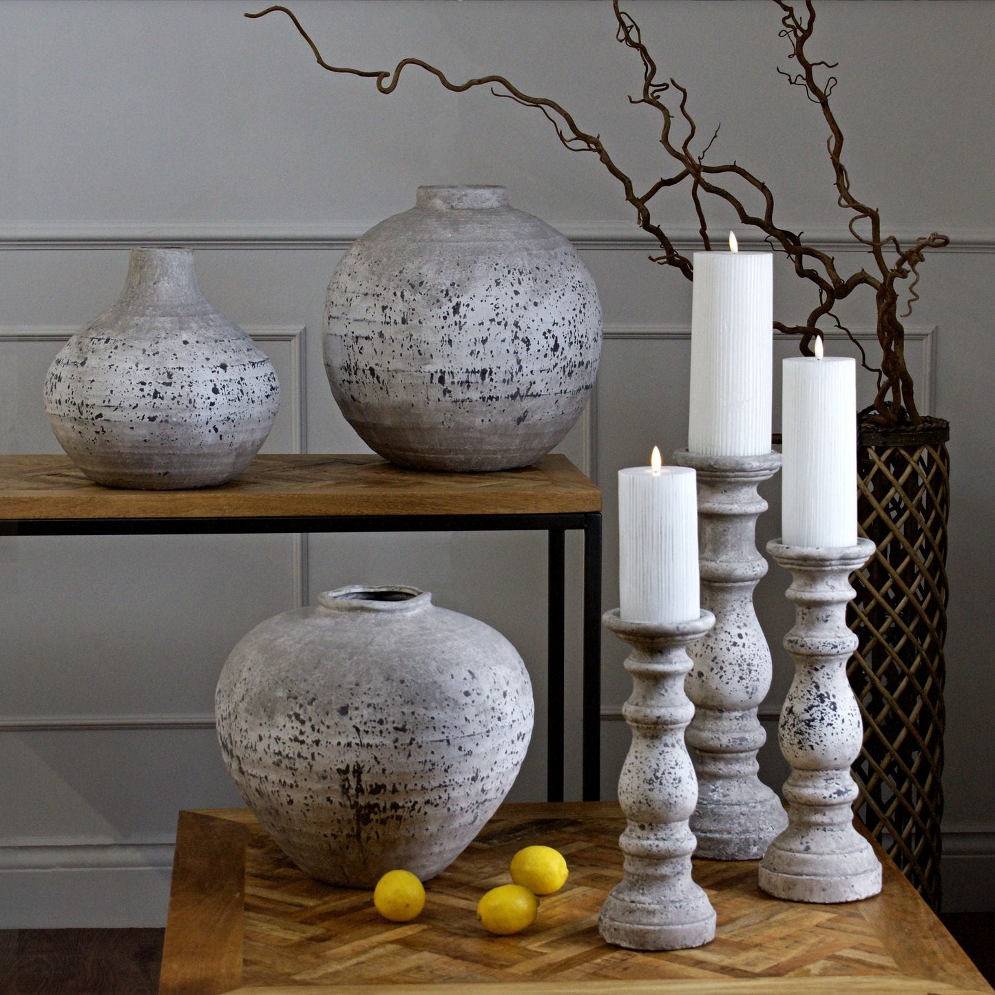 Aged stone regal vase on coffee table in the foreground, and 3 matching candlesticks. On a console table behind are 2 vases