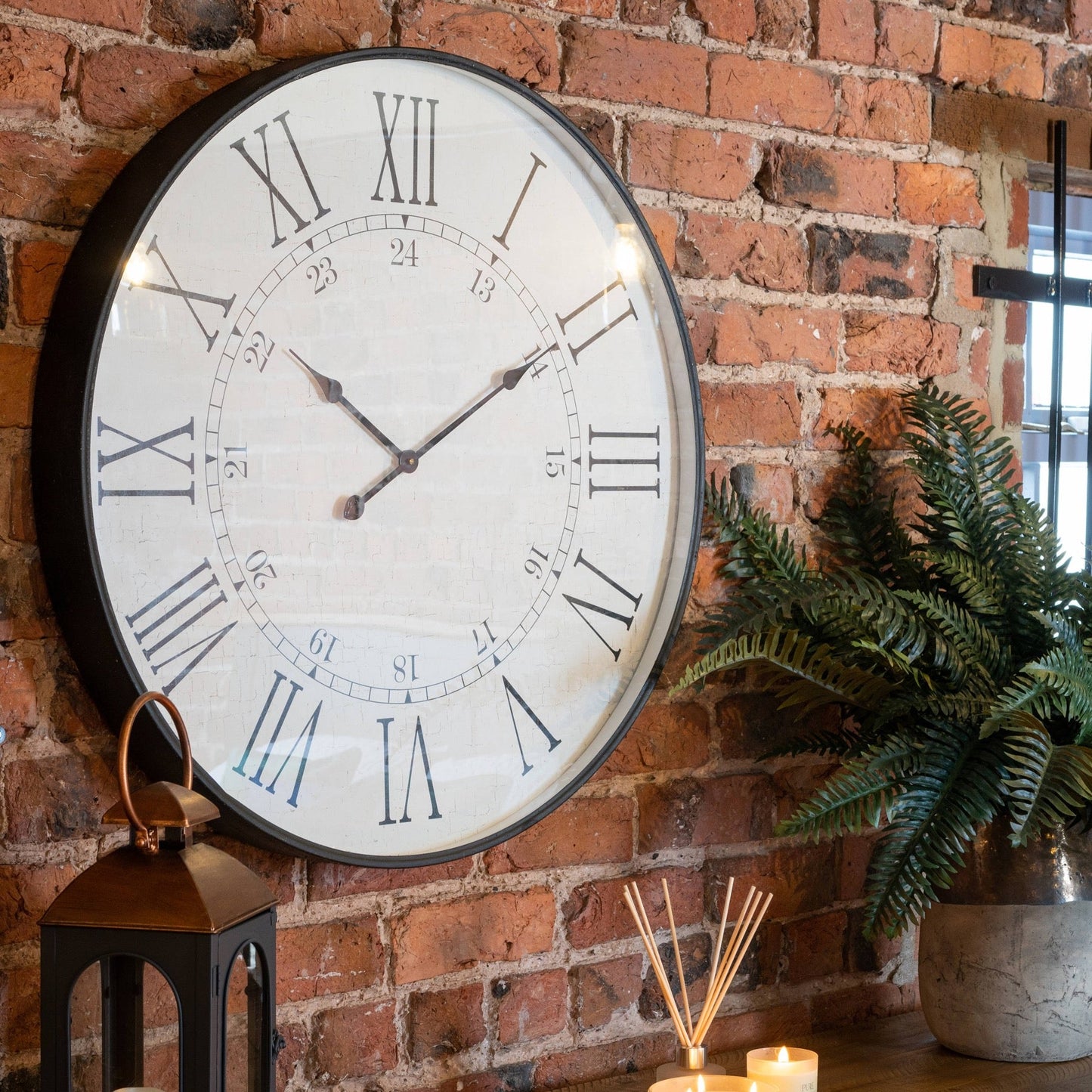 station clock on exposed brick wall. Artificial plant to the right, decorative items to the left