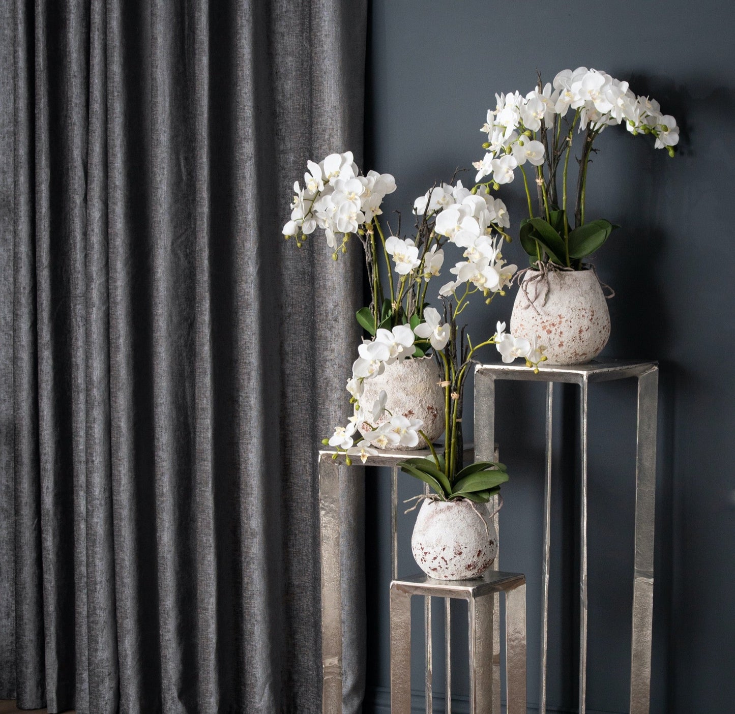 white orchids in stone pots, varying sizes on silver side tables