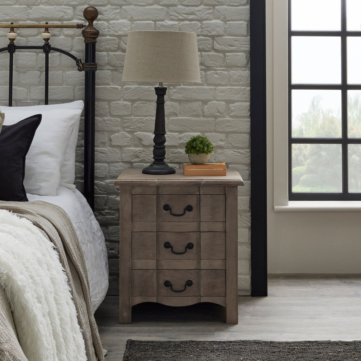 bedside next to bed, with lamp on top and small artificial plant