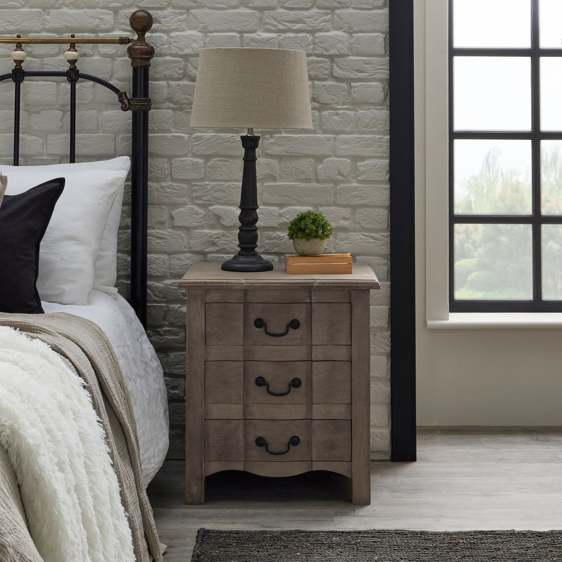 bedside next to bed, with lamp on top and small artificial plant