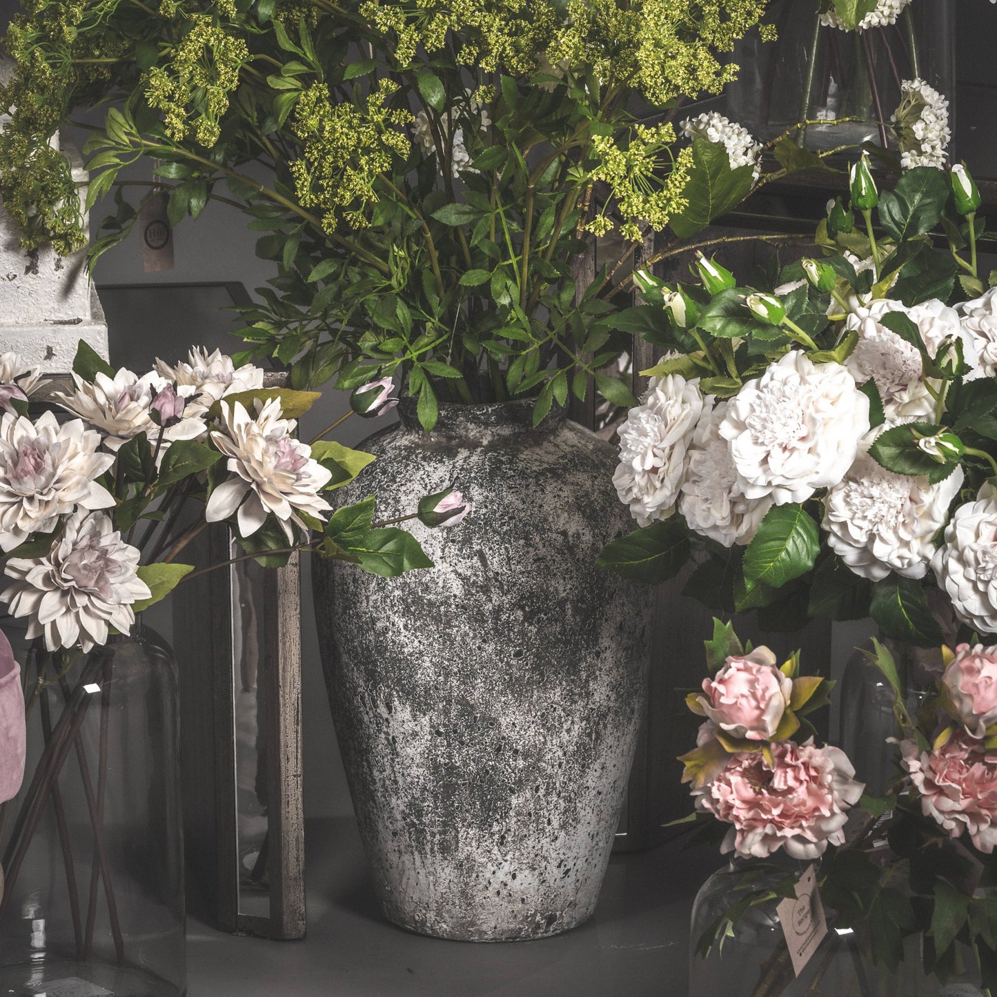 Aged stone vase lifestyle image with green foliage in surrounded by other artificial flowers