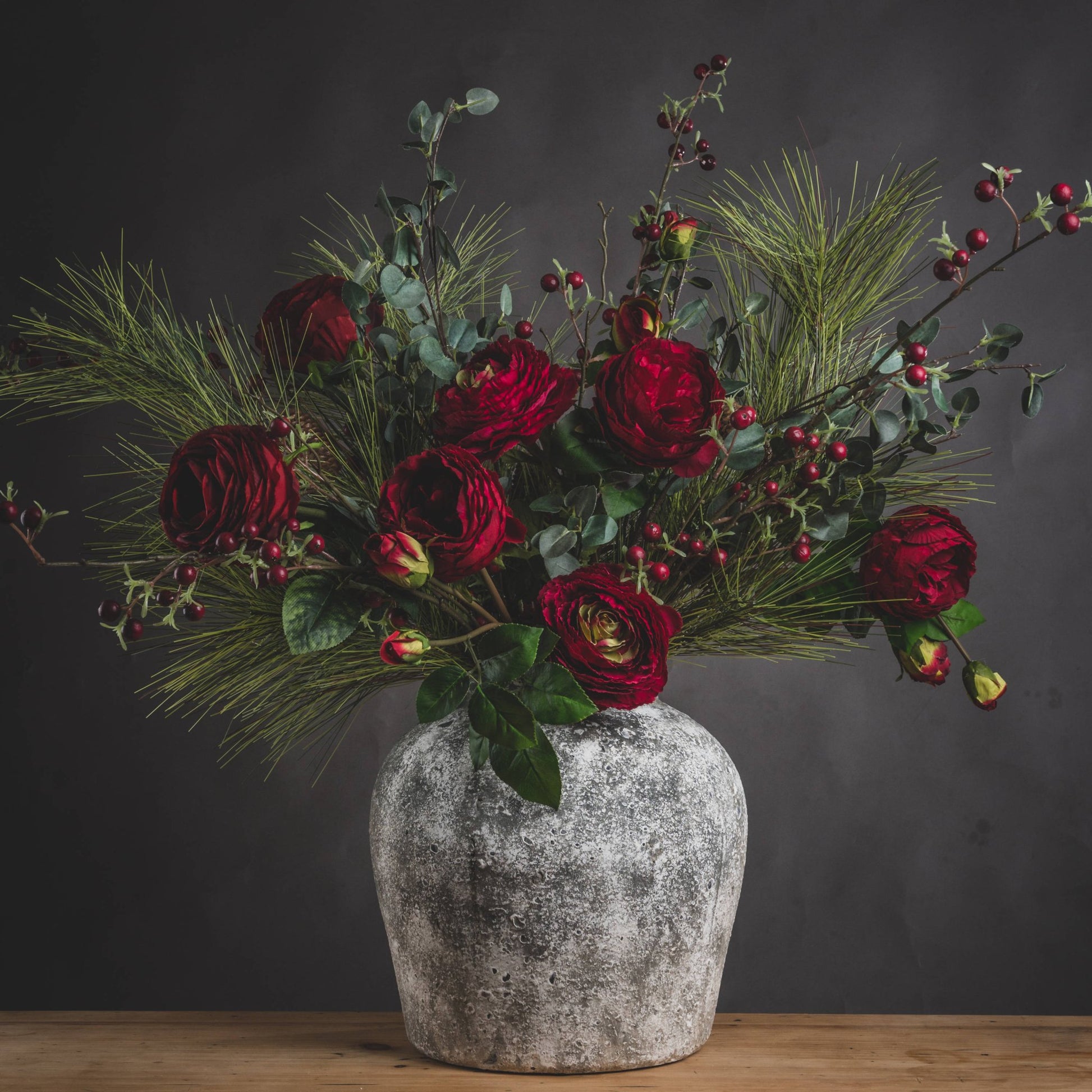 Aged stone vase with artificial deep red roses in and green foliage