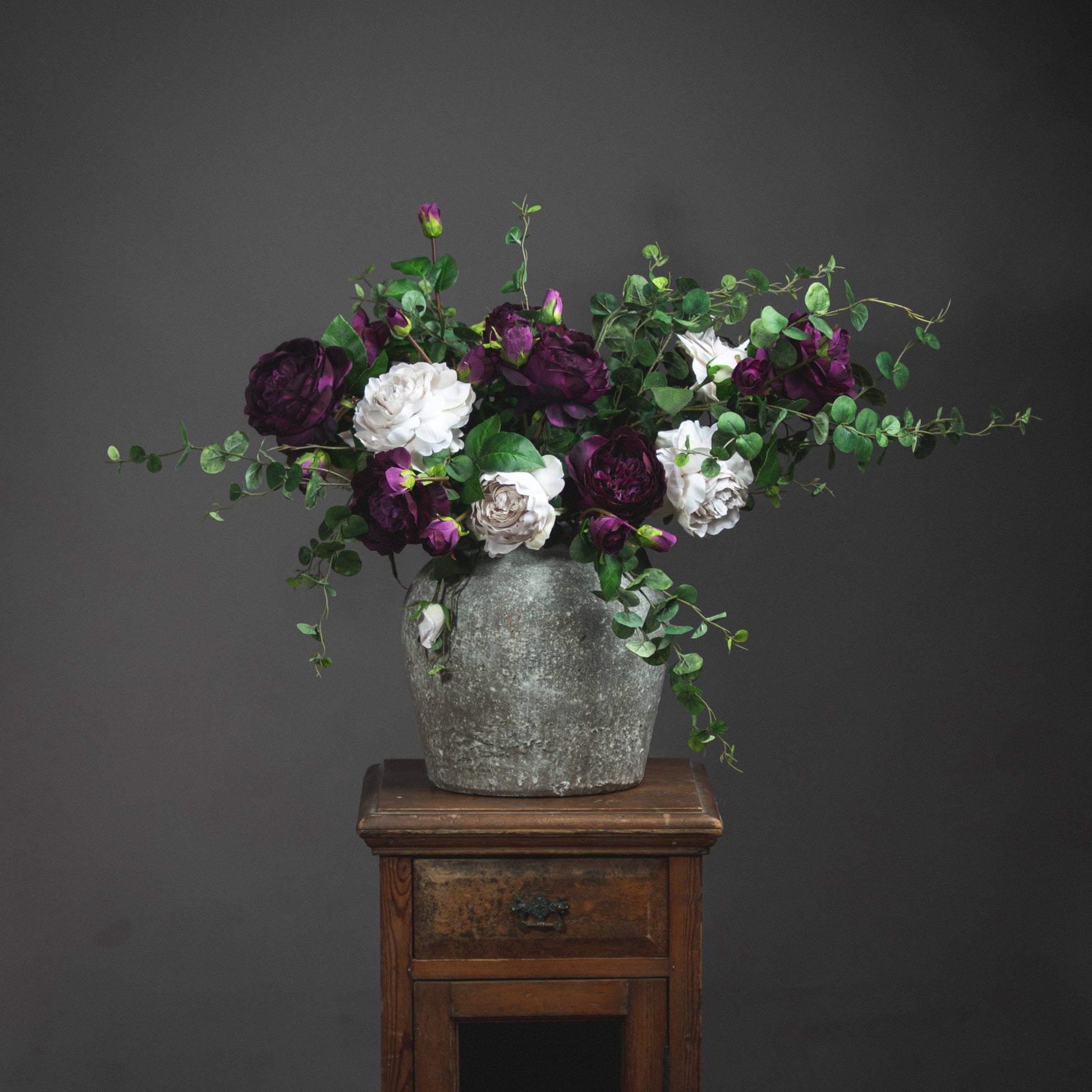 Aged stone vase with artificial deep red and cream roses in and green foliage