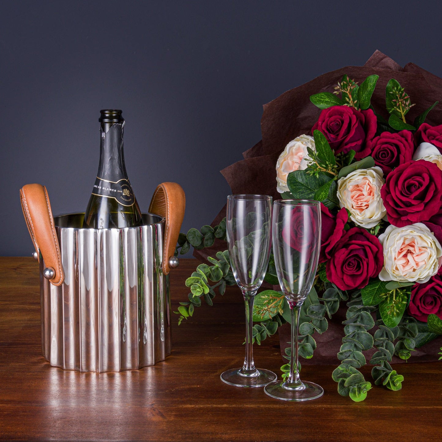 champagne bucket next to two champagne glasses in front of a bunch of red and pink roses