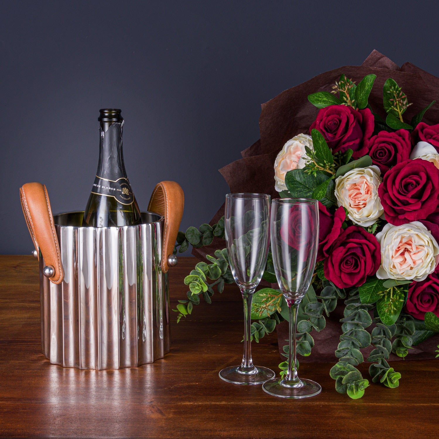 champagne bucket next to two champagne glasses in front of a bunch of red and pink roses
