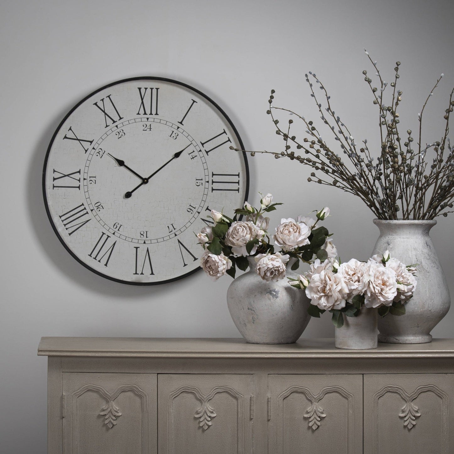 station clock above white washed sideboard with three varying size stone vases 