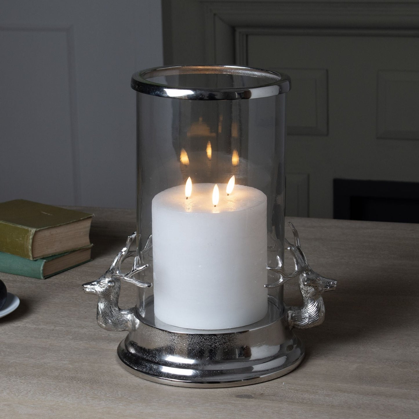 lifestyle image of Stag Head Hurricane Lantern with Triple Wick LED Candle in, two green leather bound books are in the background